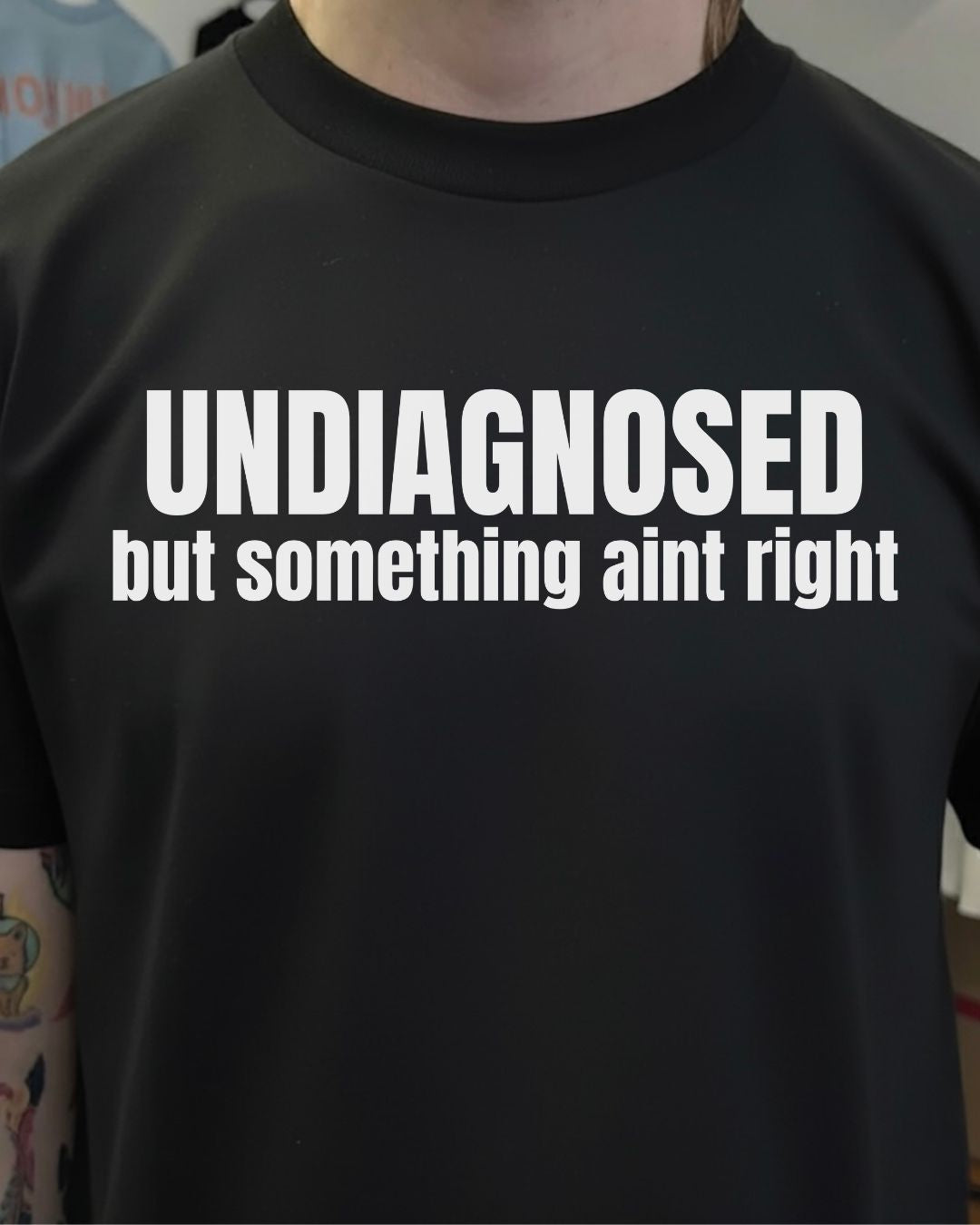 Black t-shirt with white text 'UNDIAGNOSED but something aint right' worn by a person.